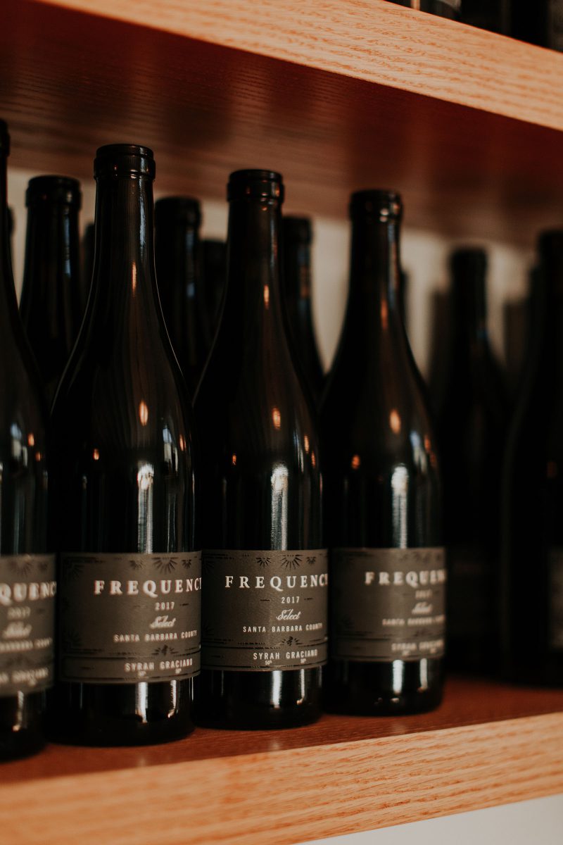 a dozen or so bottles of Frequency Select 2017 Graciano Syrah on a shelf at our tasting room in Santa Barbara