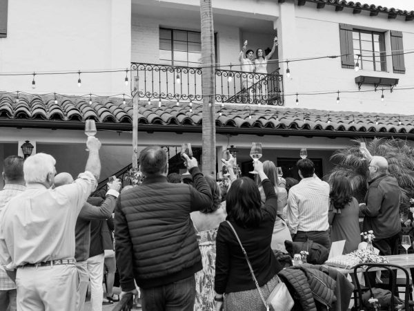 A view of Collen & Christian on the balcony overlooking the crowd at their Wedding Reception in the courtyard at Frequency Wine Company in Santa Barbara, California